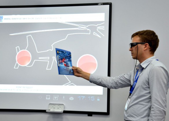 Менеджер по развитию проекторного бизнеса Александр Думанский демонстрирует работу специального приложения, которое, распознав изображение вертолета, выводит на экран очков цифровую информацию об устройстве и технических характеристиках машины